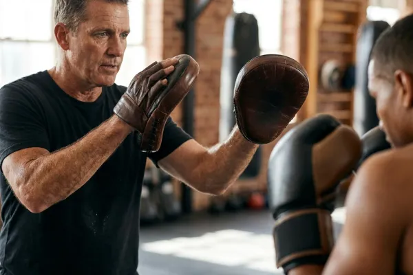 Entrenador de boxeo sujetando manoplas curvas de cuero para una sesión de precisión y golpeo